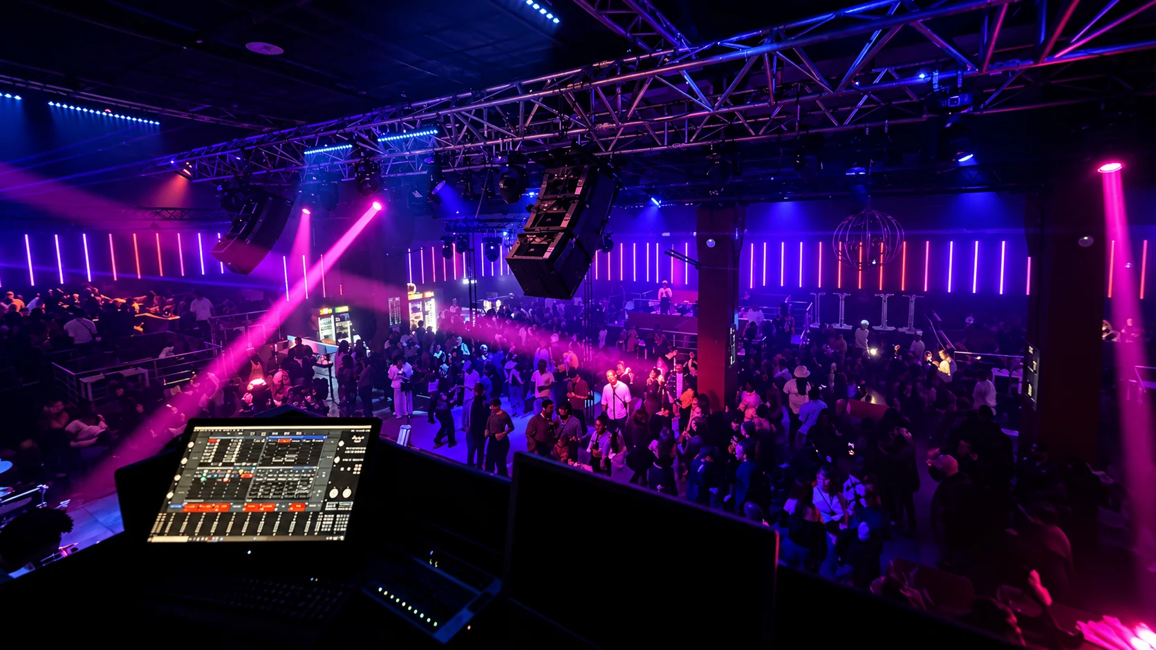 Blick vom FOH-Platz über ein digitales Mischpult auf Publikum und beleuchtete Live-Produktion.